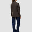 Eine Person, von hinten gesehen, die einen Women Serene Blazer Regular Walnut Herringbone, eine dunkelblaue Jeans und braune Schuhe trägt.