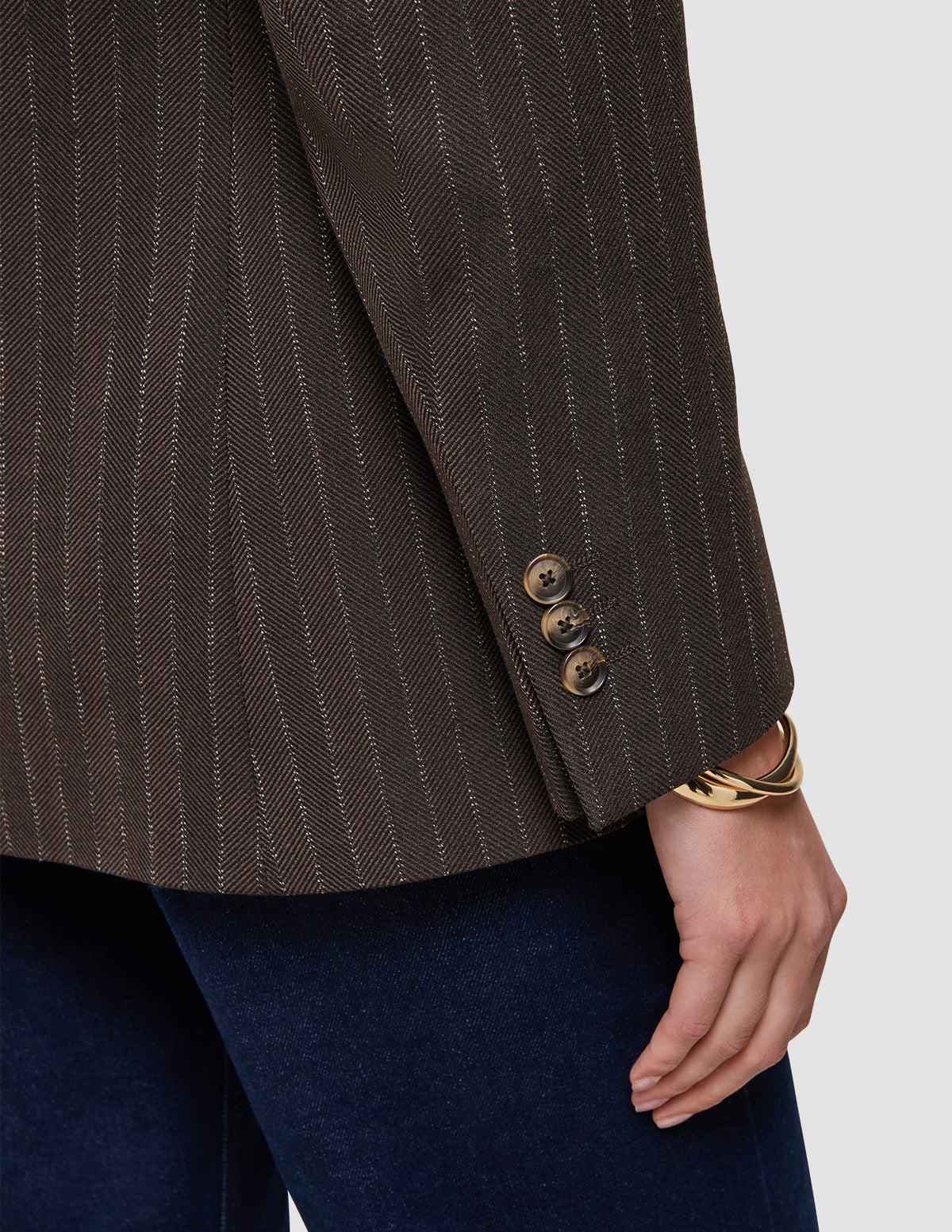 Nahaufnahme eines Women Serene-Blazers in der Passform Regular in der Farbe Walnut mit Fischgrätenmuster am Ärmel, brauner Fischgrätenstruktur in Wolloptik, drei Knöpfen an den Manschetten und einem goldenen Armreif am Handgelenk.