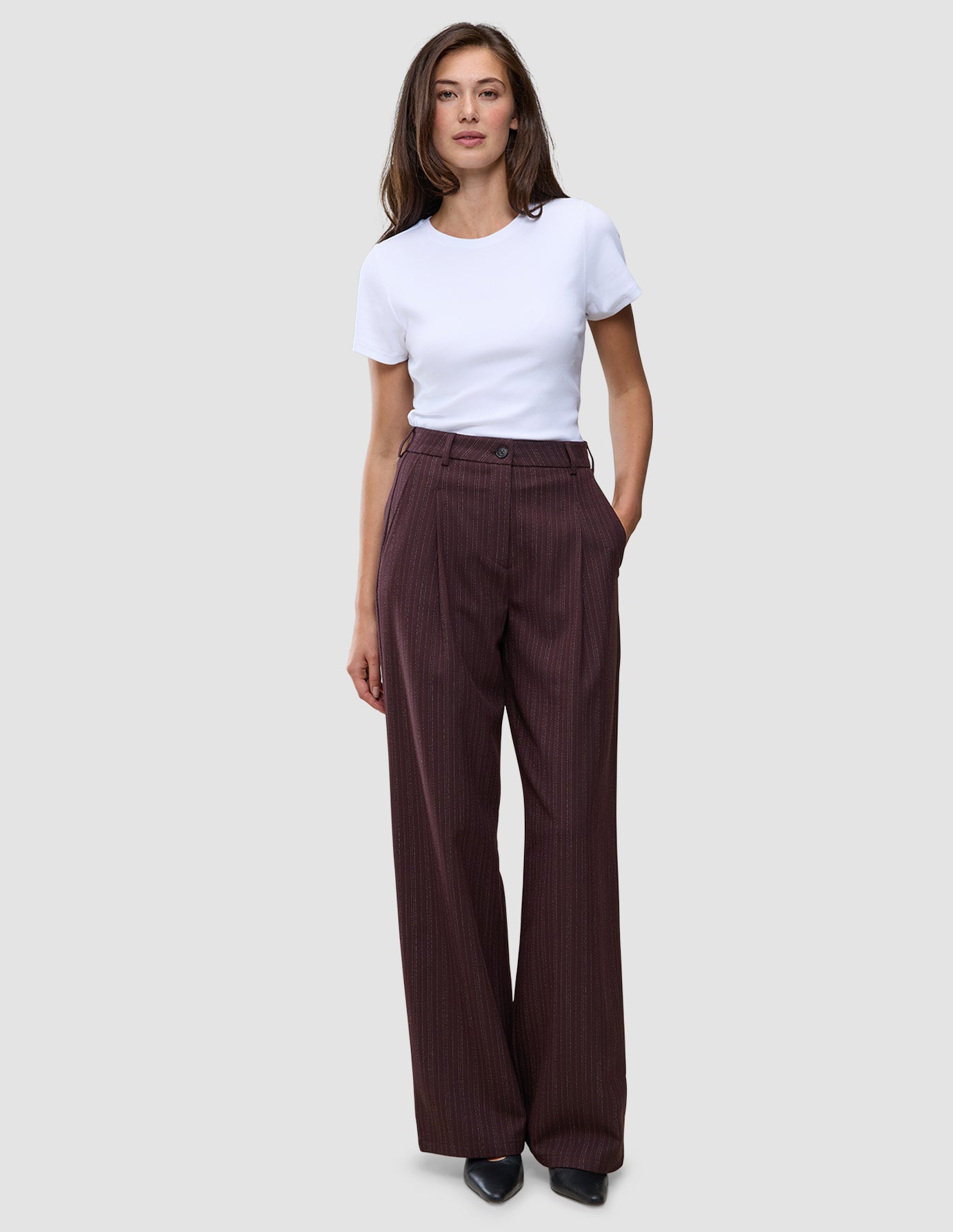 Eine Frau trägt ein weißes T-Shirt und eine burgunderrote, weit geschnittene Hose mit Nadelstreifen – das Modell Women Serene Pants Wide Berry Pinstripe.