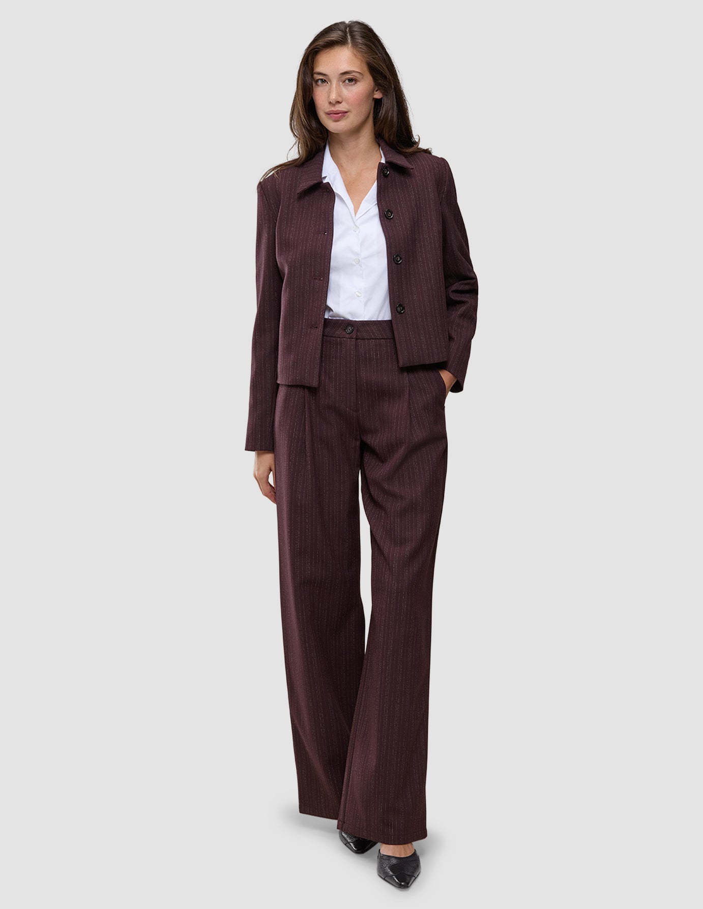 Eine Frau, die einen Anzug der Marke Women Serene Pants Wide Berry Pinstripe mit weitem Hosenbein über einem weißen Hemd trägt.