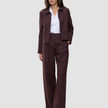 Eine Frau, die einen Anzug der Marke Women Serene Pants Wide Berry Pinstripe mit weitem Hosenbein über einem weißen Hemd trägt.