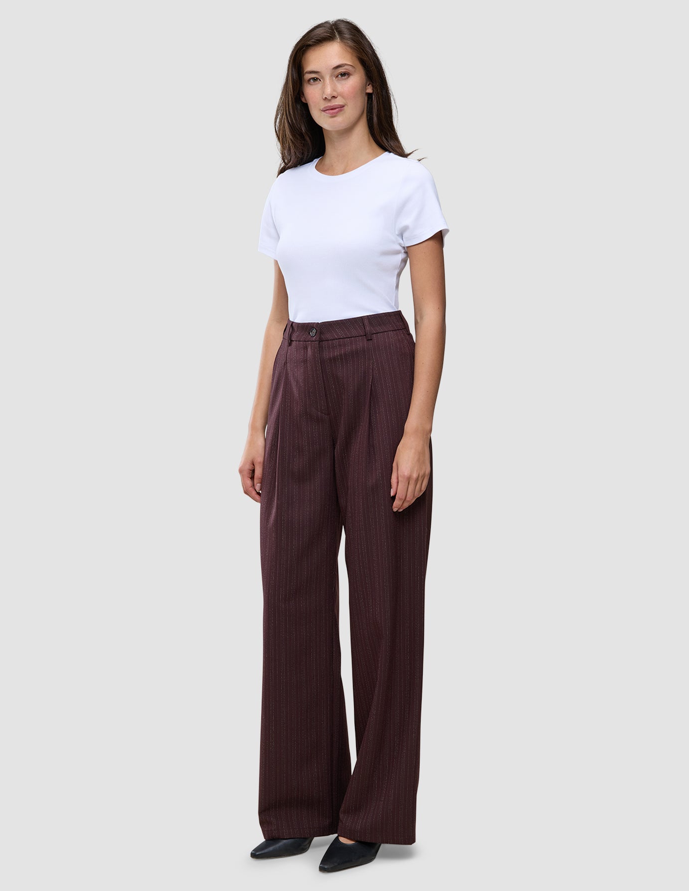 Eine Frau trägt ein weißes T-Shirt und eine weit geschnittene Women Serene-Hose in einem dunklen Beerenfarbton mit dezentem Nadelstreifenmuster.