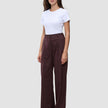 Eine Frau trägt ein weißes T-Shirt und eine weit geschnittene Women Serene-Hose in einem dunklen Beerenfarbton mit dezentem Nadelstreifenmuster.
