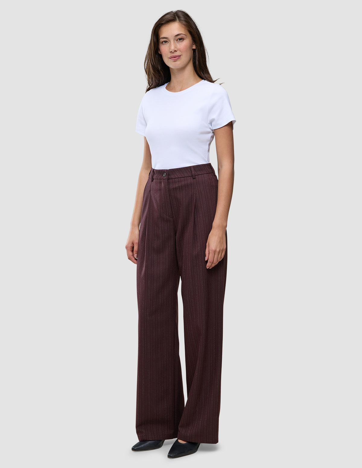 Eine Frau trägt ein weißes T-Shirt und eine weit geschnittene Women Serene-Hose in einem dunklen Beerenfarbton mit dezentem Nadelstreifenmuster.