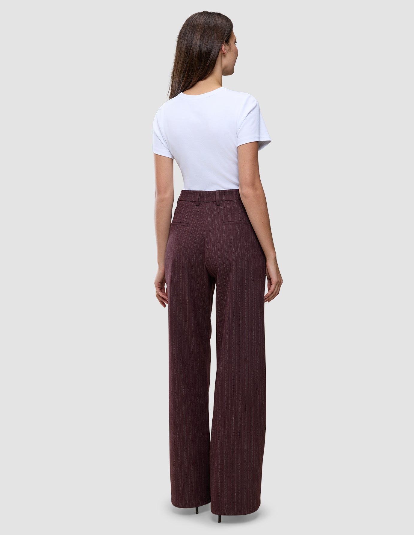 Rückansicht einer Person, die eine hoch taillierte, weit geschnittene Women Serene Pants Wide Berry Pinstripe trägt, kombiniert mit einem weißen T-Shirt, das skandinavisches Design verkörpert.