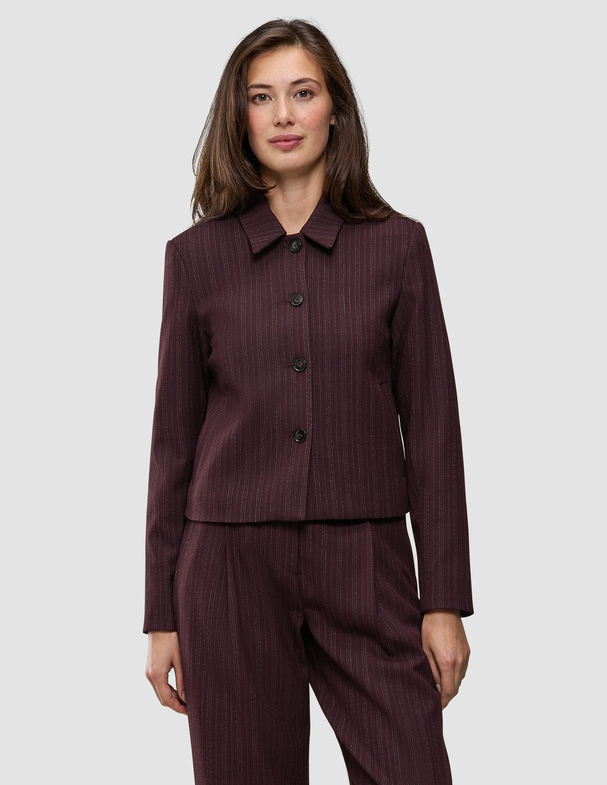 Eine Frau trägt die Women Serene Short Jacket Berry Pinstripe – eine Jacke aus dunkelviolettem Stoff mit Nadelstreifen, die sich durch eine kastenförmige Passform und eine kurze Silhouette auszeichnet.