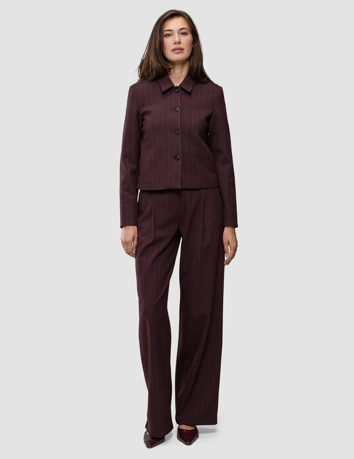 Eine Frau, die die kurze Damenjacke Serene in Berry Pinstripe und eine dazu passende Hose mit weitem Bein im minimalistischen skandinavischen Stil trägt.
