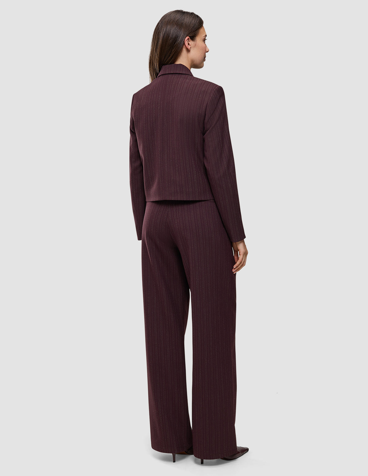 Eine Person, von hinten gesehen, trägt die kurze Damenjacke Serene in der Farbe Berry Pinstripe mit kastenförmiger Passform sowie eine dazu passende Hose mit weitem Bein im skandinavischen Stil.