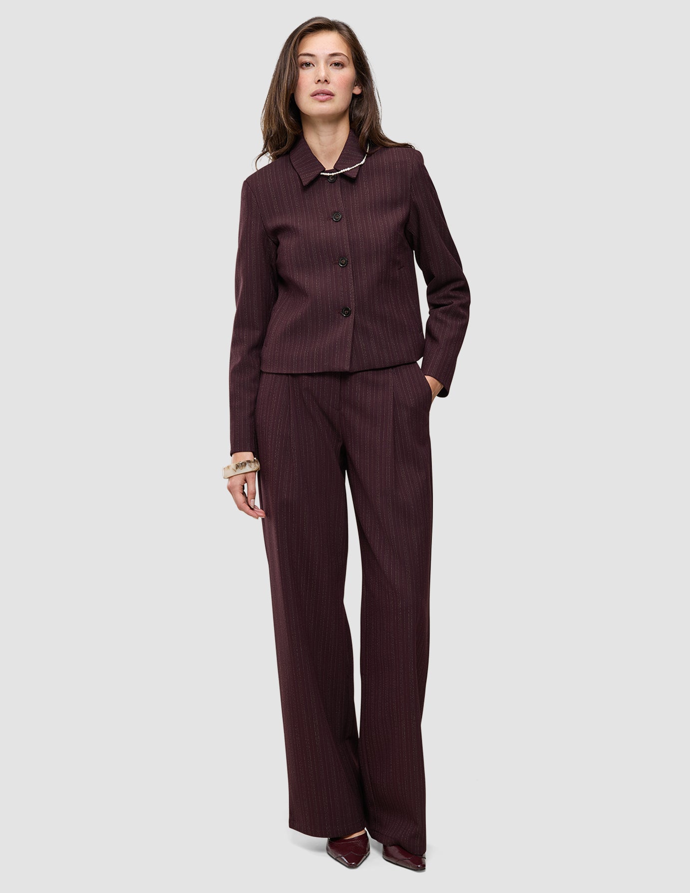 Eine Frau trägt eine kurze Damenjacke Serene in der Farbe Berry Pinstripe mit kastenförmiger Passform und dazu passende Hosen mit weitem Bein im skandinavischen Design.
