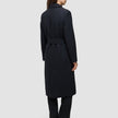 Eine Frau wird von hinten gezeigt. Sie trägt einen schwarzen Damenmantel aus Wolle in minimalistischem skandinavischem Design mit einer langen Silhouette und Gürtel.